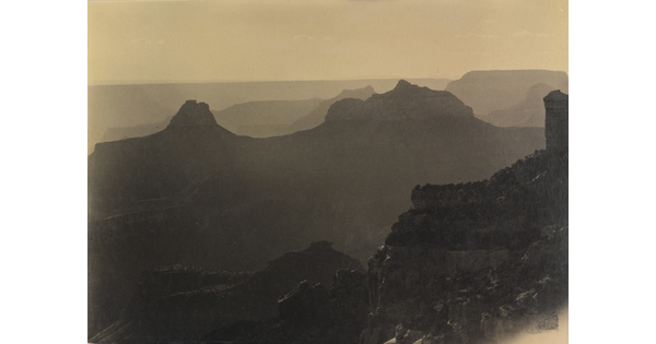 A sepia-toned photograph of the silhouettes of mesas, rock formations, and distant mountains.