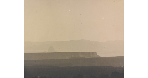 A sepia-toned photograph of a hazy mesa and distant mountains.
