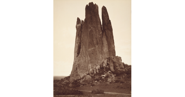 A sepia-toned photograph of a large vertical rock formation against a clear sky.