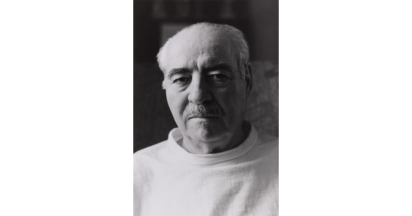 A black-and-white portrait photograph of an older, balding White man with dark eyebrows, a mustache, wearing a light shirt.