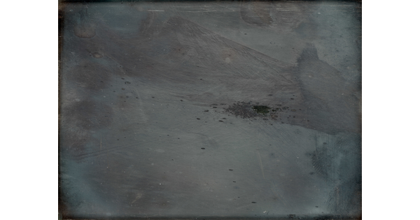 An obscured black-and-white photograph of gray, monochromatic forms, including an angular shape across the top right corner and a splatter in the center.