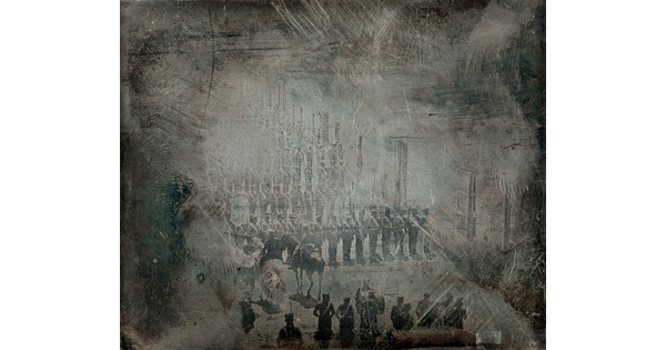 A dark, heavily scratched black-and-white photograph of rows of soldiers facing two figures on horseback and another group of soldiers.