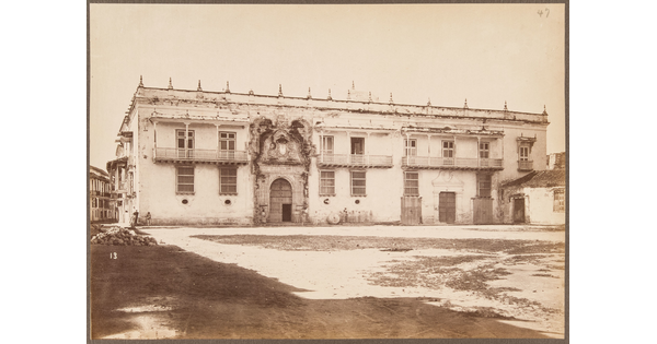 A sepia-toned photograph of an intimidating two-story structure, awash in light, with an ornate entrance and spikes across the top.