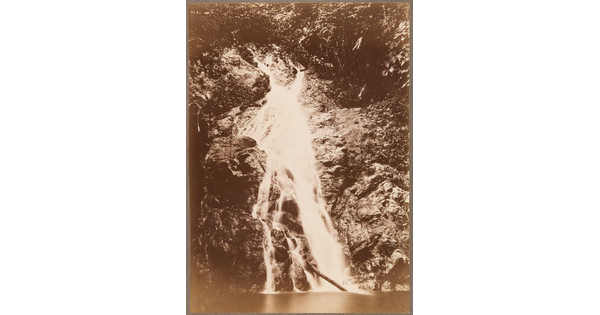 A sepia-toned photograph of a waterfall going down a rocky hill toward a river.