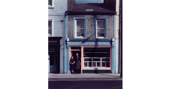 A color photograph of a White man and woman standing in the doorway of a small, two-story storefront.