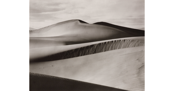 A black-and-white photograph of rolling sand dunes.