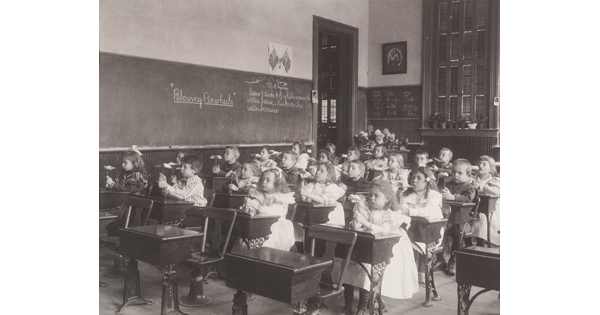 A black-and-white photograph of a classroom of young children seated at desks blowing on pinwheels.