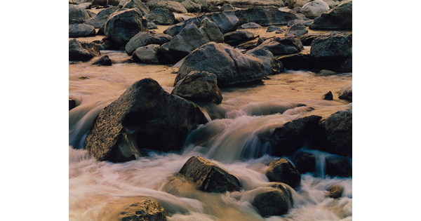 An up-close color photograph of water rushing over rocks in a river.
