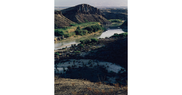 A color photograph of a winding river surrounded by rocky cliffs and vegetation.