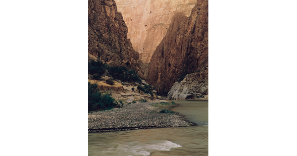 A color photograph of a river surrounded by tall rocky cliffs with some green vegetation.