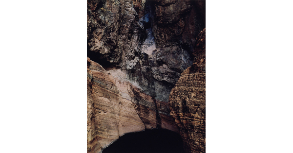 A color photograph of the side of a rocky cliff showing layers of rock above a dark hole.