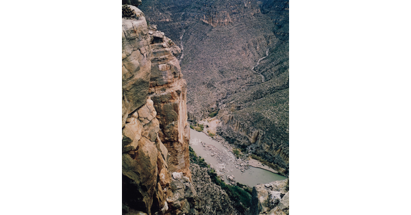 A color photograph taken from the top of a cliff overlooking a river surrounded by other rocky cliffs.