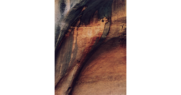 A color photograph of a multi-toned, mostly smooth cliff face.