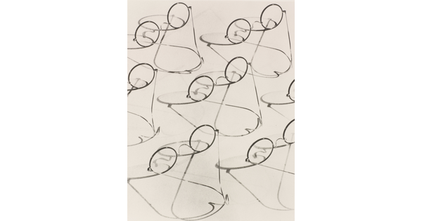 A black-and-white photograph of multiple granny-style eyeglasses and their shadows.