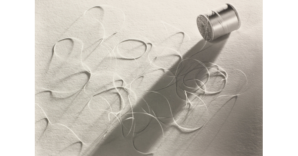 A black-and-white photograph of a spool of thread laying on its side with loose thread in loops around it.