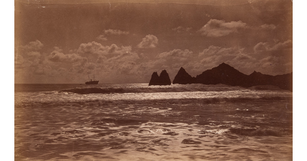 A sepia-toned photograph of a boat heading toward a rocky coast on an ocean.