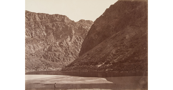 A black-and-white photograph of a person standing in a river surrounded by large rocky mountains.