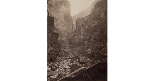 A black-and-white photograph of the bottom of a rocky canyon surrounded by tall cliffs.