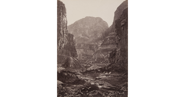 A black-and-white photograph of the bottom of a rocky canyon surrounded by tall cliffs.