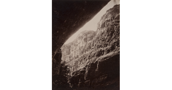 A black-and-white photograph of a steep cliff face from underneath a rock overhang.