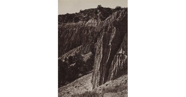 A black-and-white photograph of rocky cliffs jutting up from a desert landscape.