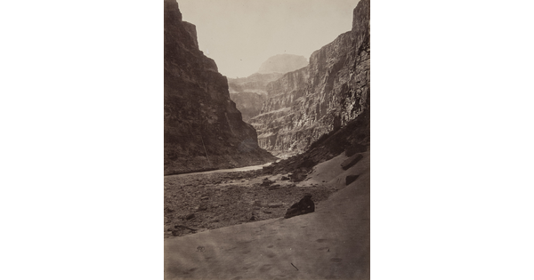 A black-and-white photograph of a river running through a canyon surrounded by tall cliffs.