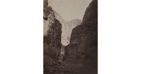 A black-and-white photograph of tall rocky canyon walls taken from the ground looking up.