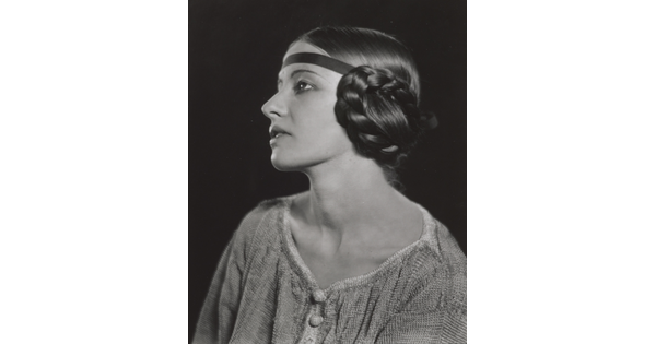 A black-and-white portrait of a White woman in profile with braided hair covering her ear.