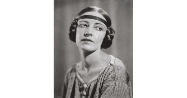 A black-and-white portrait of a White woman with her hair braided into buns on the sides of her head.