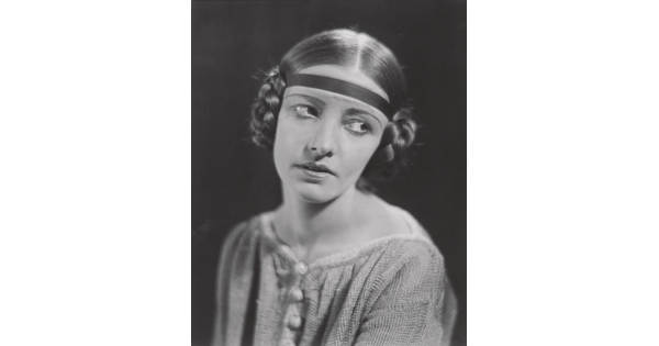 A black-and-white portrait of a White woman, eyes looking to the side, with her hair braided into buns on the sides of her head.