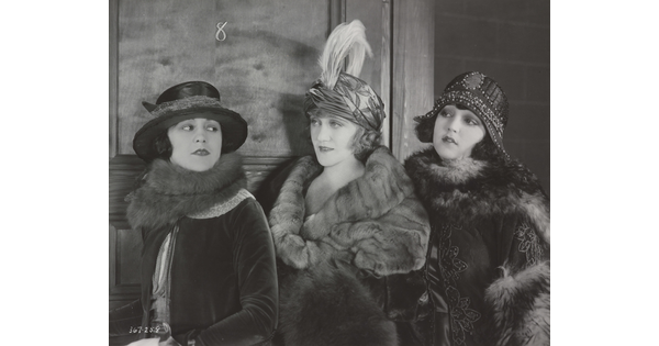 A black-and-white photograph of three elaborately-dressed White women, all wearing hats and fur stoles.