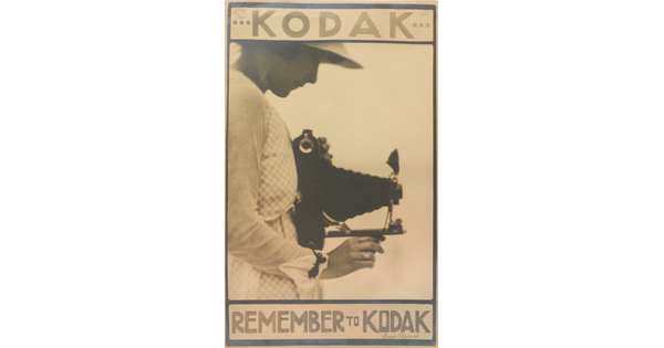 A sepia-toned advertisement poster for Kodak of a White woman in profile holding a large camera and looking down into the viewfinder.