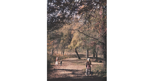 A color photograph of two adults and one child walking on a dirt road under autumn-colored trees.