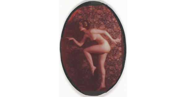 A faded color oval-shaped photograph of a nude, fair-skinned women posed as if in the middle of a dance, with one leg bent, arms out, and yellow flowers in her hair.