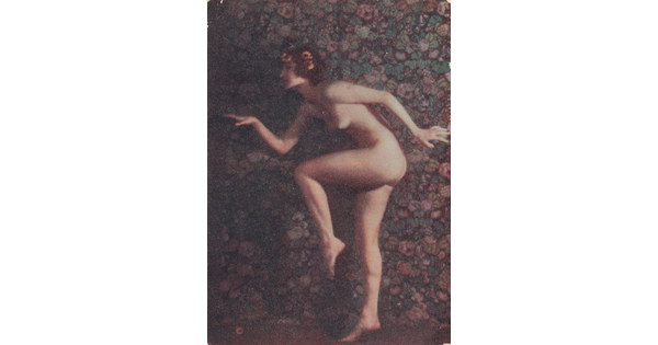 A faded color photograph of a nude, fair-skinned women posed as if in the middle of a dance, with one leg bent, arms out, and yellow flowers in her hair.