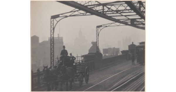 A black-and-white photograph of a horse-drawn carriage crossing a bridge next to streetcar rails as haze obscures buildings in the background.