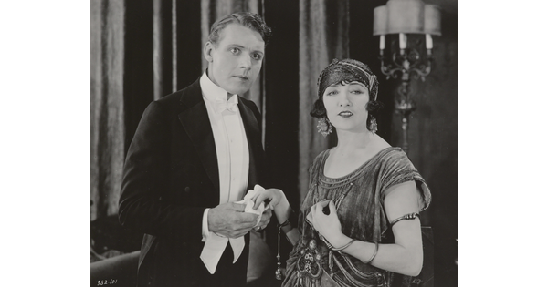 A black-and-white photograph of a White woman and a White man, both elegantly dressed and looking at something in the distance.