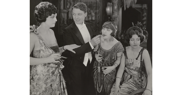 A black-and-white photograph of three White women and one White man, all elaborately dressed and engaged in conversation.