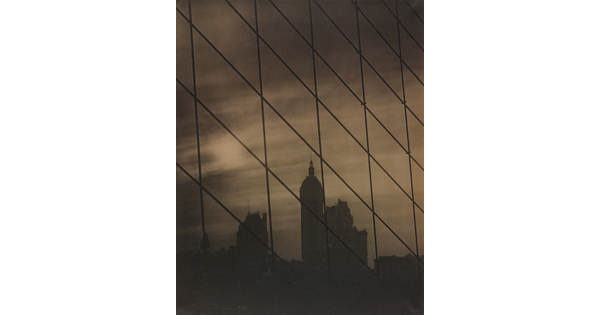 A sepia-toned photograph of a patterned grid of cables in front of a dark city skyline.
