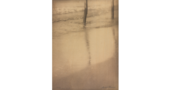 A sepia-toned photograph of water washing on a sandy beach around two poles in the top left corner.