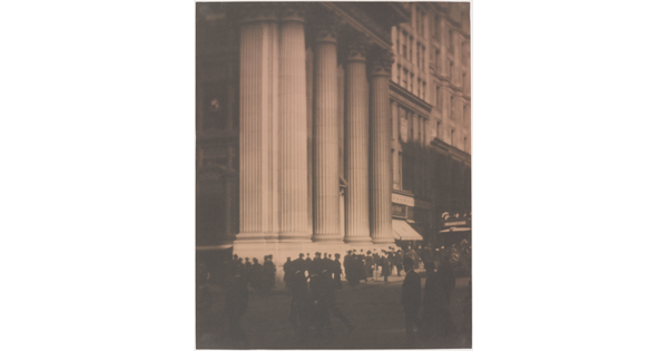 A sepia-toned photograph of people walking in front of a tall white city building with large fluted columns.