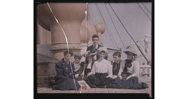 A color photograph of a group of young, fair-skinned, adults sitting on the sunny deck of a ship.