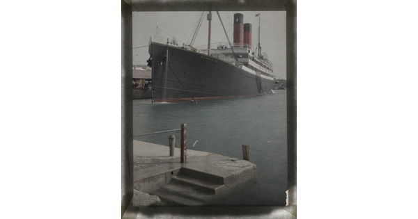 A color image large ship with red smokestacks docked in a harbor.