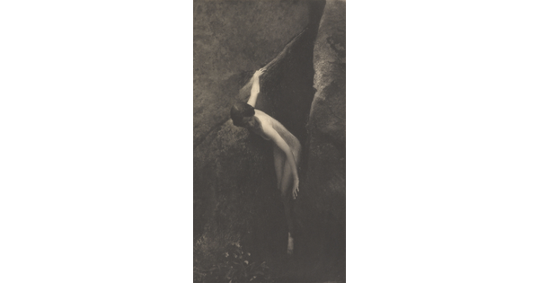 A sepia-toned photograph of a nude White woman emerging from between two large boulders.