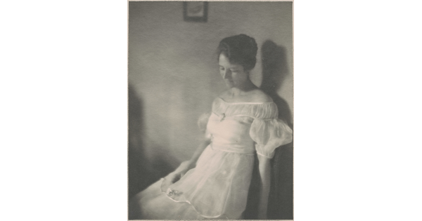 A black-and-white photograph of a seated White woman with dark hair in an up-do wearing a white ruffled dress.