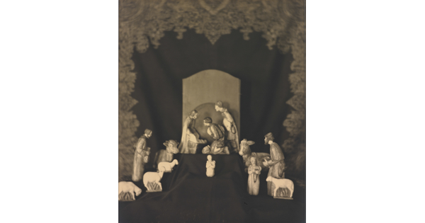 A sepia-toned photograph of human and animal figurines assembled on a black fabric background in a nativity scene.