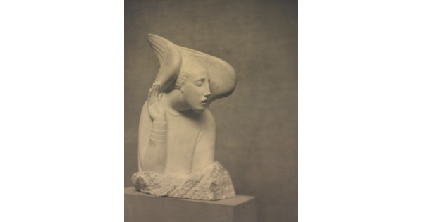 A sepia-toned photograph of a white stone sculpture of an abstracted human figure with wings around the sides of its head.