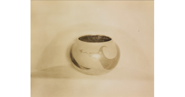 A sepia-toned photograph of a spherical bowl with abstract animal designs on a light background.