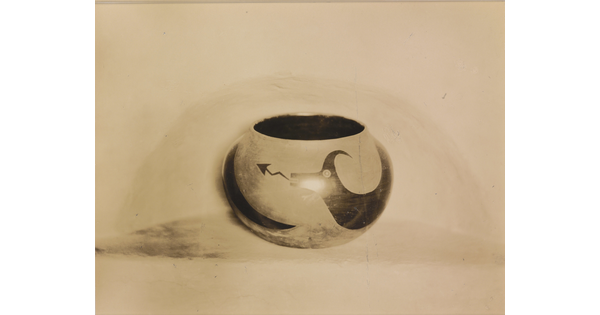 A sepia-toned photograph of a spherical bowl with abstract animal designs on a light background.