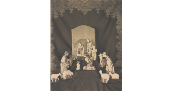 A sepia-toned photograph of human and animal figurines assembled on a black fabric background in a nativity scene.